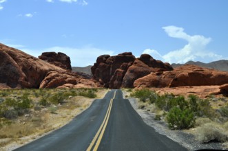 Lonely road leads through red rocky landscape in the desert under blue sky with clouds, Valley of