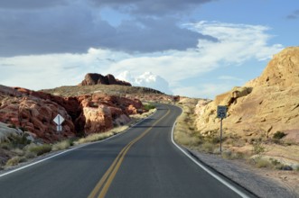 Narrow road with road sign snakes through red rocks under dramatic clouds in the sky, Valley of