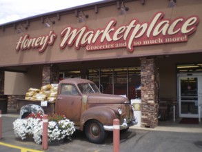 Old Studebaker pickup truck full of flowers parked in front of a nostalgic market building, Honey's