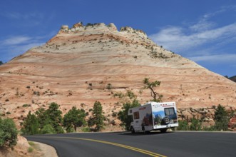 Motorhome drives along a road framed by red rocks and clear skies, Zion National Park, Utah, USA