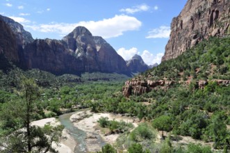 River flows through a lush valley surrounded by imposing mountains and green vegetation, Zion