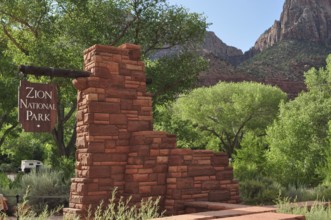 Brick monument with sign in Zion National Park, surrounded by green trees and mountains, Zion
