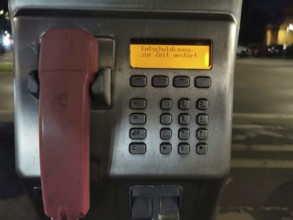 Public telephone at night, display shows error message, sorry currently disturbed, urban area,