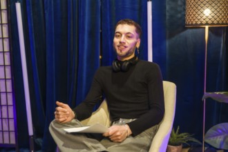 Young man wearing headphones around his neck and holding papers. Actively engaging. Communicating.