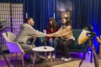 Three young content creators, a man and two women, smiling and shaking hands during a podcast