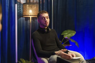 Young man wearing headphones around his neck, actively discussing a topic while recording content