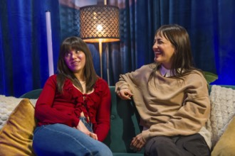 Two cheerful young women are having a conversation and laughing while creating content for a