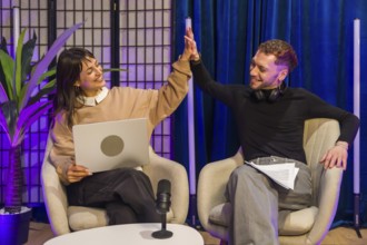 Two smiling content creators high fiving during a successful recording session in a modern podcast