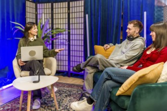 Young diverse creators recording a podcast in a stylish studio, chatting around microphones and