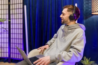 Young man creating digital content, recording a podcast or live stream, smiling and using a laptop
