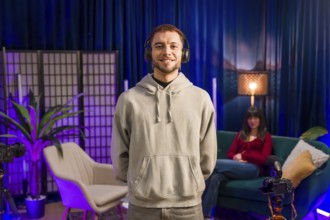Content creator standing and smiling, wearing headphones in a modern recording studio setup with a