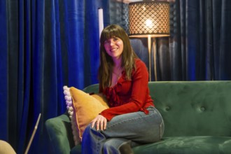 Young smiling woman sitting on a green couch in a contemporary recording studio, engaged in content