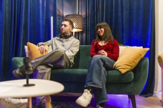 Young man and woman sitting on a green sofa, actively listening and engaging while recording a