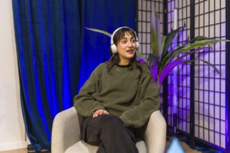 Young woman in a modern home studio wearing headphones, hosting a podcast or livestream, speaking