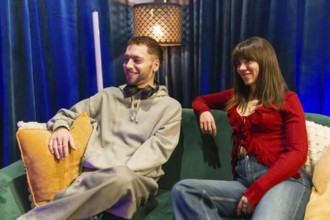 Young man and woman sitting on a green couch, sharing ideas and smiling during a social media