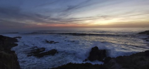 Dramatic sunset with dark clouds and waves, rocks in the foreground, hiking on the Fisherman's