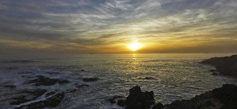 The picture shows an atmospheric sunset over the sea with dramatic clouds, hiking on the