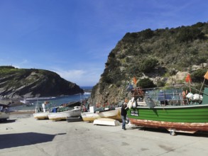 Small harbor with colorful fishing boats against a rocky coastal backdrop, hiking on the