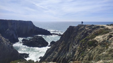 Rocky outcrop with person looking out at the vast open sea and imposing rock cliffs hiking on the