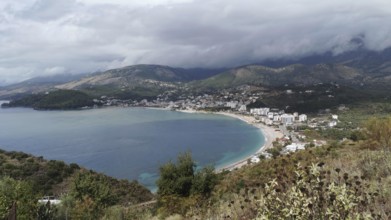 Coastal town in a bay surrounded by mountains and under a cloudy sky, Himare, Albanian Riviera,