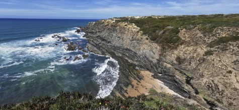 Coastal landscape with eroded rock formations and breaking waves on a sandy beach, hiking on the