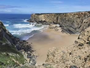 Secluded bay with golden sandy beaches and breaking waves between steep cliffs, hiking on the