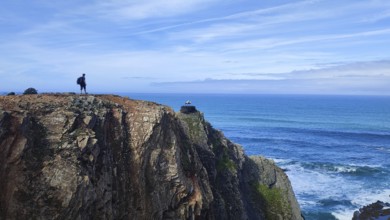 Lone hiker on rocky cliff overlooking the vast ocean, stork's nest (ciconia), Fisherman's trail,