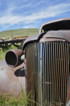Close-up of a rusty car wreck, Chevrolet Coupé, against blue sky and green area, Bodie Ghost Town,