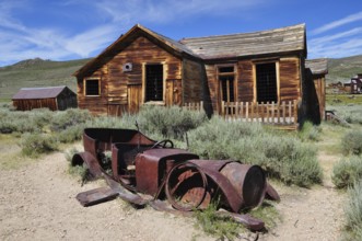 Old wooden house with rusty car wreck in front of it, surrounded by nature, Bodie Ghost Town,