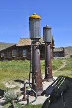 Two rusty old gas pumps, gas station, in front of a historic wooden building under a blue sky,