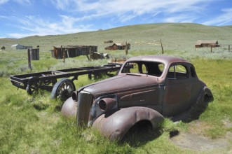 Rusty car wreck, Chevrolet Coupé, in front of historic buildings in natural setting, Bodie Ghost