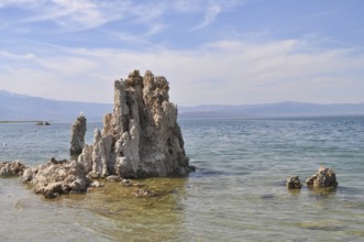 A detailed rock, Calcium Tuff Formation, rises out of the water surrounded by shore scenery, Lake