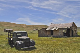 An abandoned car, vintage Ford Model 51 pickup truck, stands next to an old wooden cabin in a