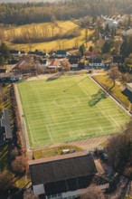 Green soccer field in rural area with surrounding trees and buildings, seen from the air, Wimberg,