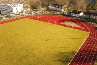 Aerial view of a sports field with red running track, yellow lawn and surrounding buildings,