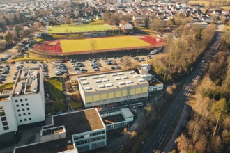 Aerial view of sports ground and school building with adjacent parking lot, nestled in an urban