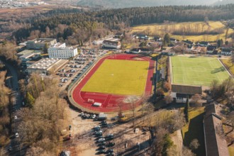 Aerial view of a sports complex with red running track and surrounding village and forest, Wimberg,