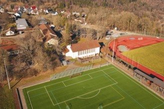 Aerial view of a sports field with red running track and nearby buildings in a village, Wimberg,