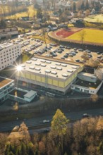 Large sports hall with sun rays and surrounding parking spaces and buildings in a winter