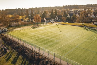 Football field is illuminated by sunlight, surrounded by village houses and trees, Wimberg, Calw,