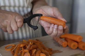 Close up of hands peeling fresh carrot on cutting board in modern kitchen. Simple ingredients,