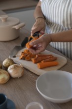 Vertical image of hands peeling carrot in modern kitchen. Casual home cooking, fresh ingredients