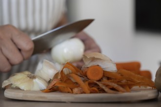 Hands peeling onion while preparing vegetables in kitchen. Casual home cooking, fresh ingredients