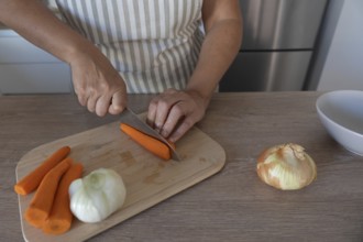 Carrot being cut with a knife on a wooden cutting board while preparing vegetables in a home
