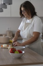 Selective focus on fresh tomatoes in foreground while woman chops onion in background. Home cooking