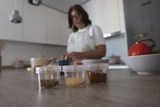 Selective focus on spices in foreground while woman chops vegetables on cutting board in background