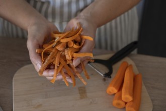 Close-up of hands holding fresh carrot peels while preparing vegetables on a wooden cutting board