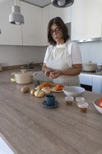 Cozy home kitchen scene with woman wearing apron peeling carrots and preparing vegetables. Comfort