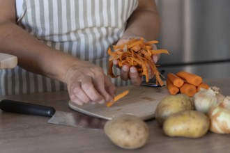 Hands holding freshly peeled carrot skins above a wooden cutting board with whole carrots and