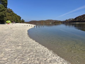 Quiet sandy beach with water views and wooded hills, Silver Sands of Morar, Mallaig, Scotland,